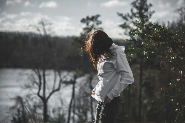 a girl standing near a lake in front of trees