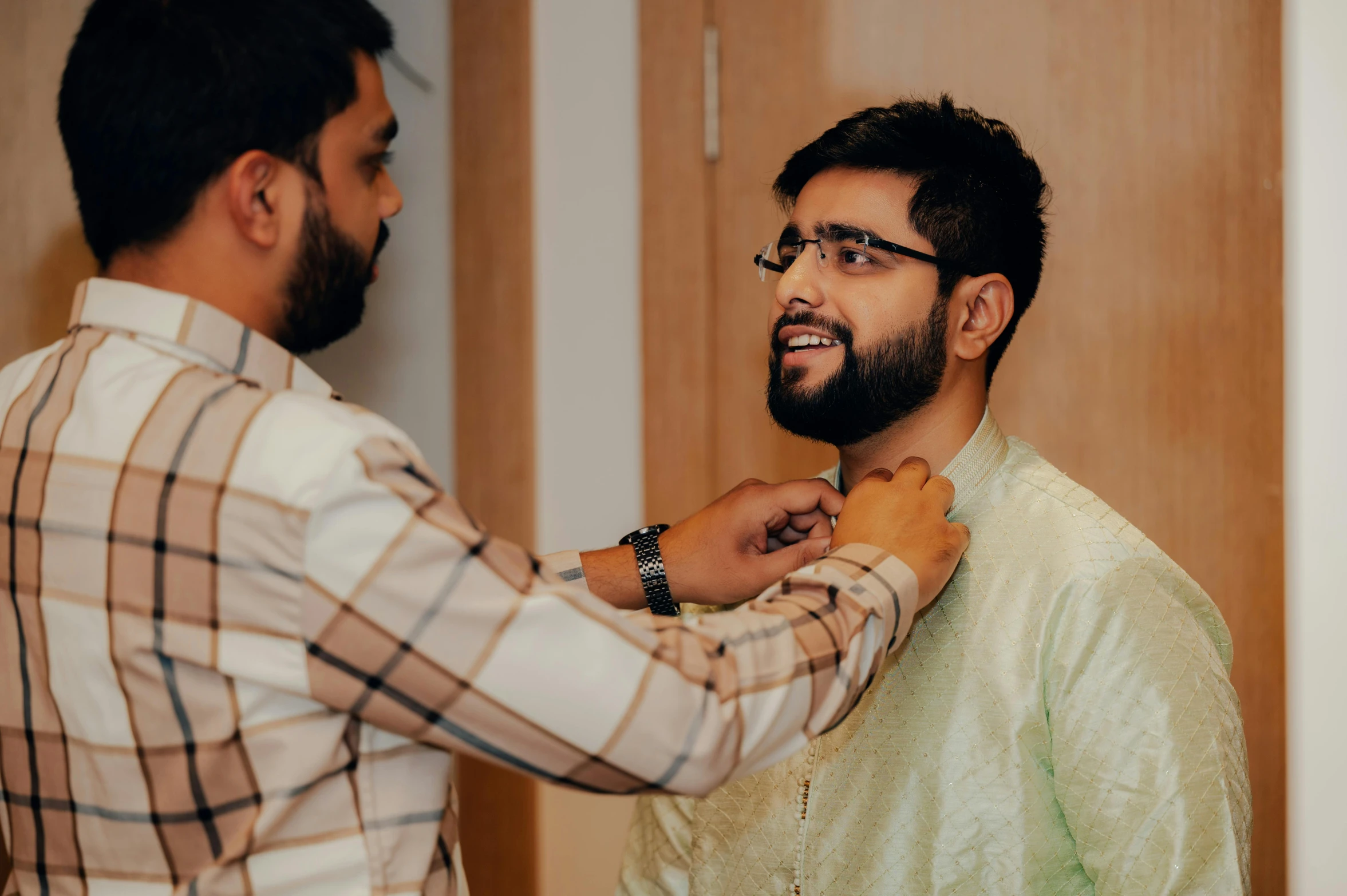 a bearded young man helps another man get his tie ready