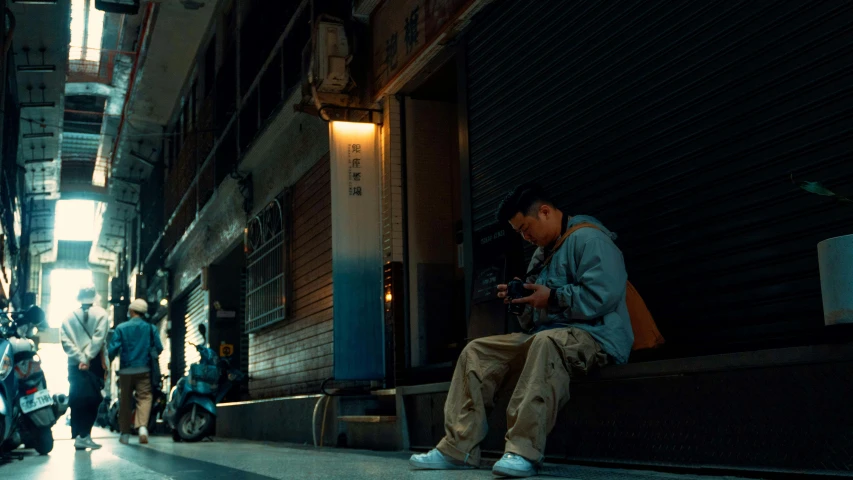 an asian man sits on the curb with a group of people in the background