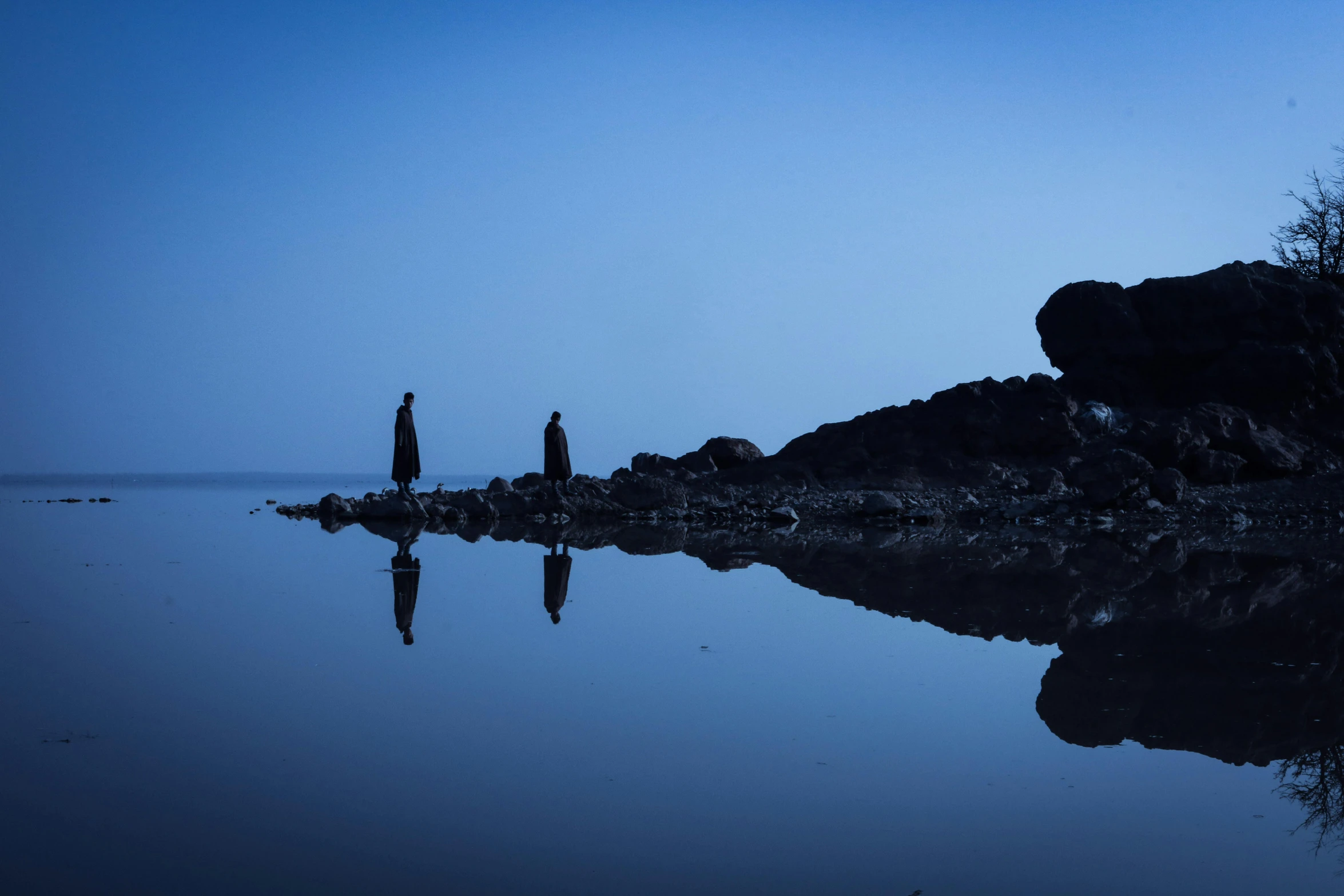 two people stand on rocks near the water