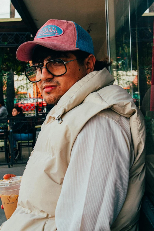 a man with glasses and a cap sitting on the street