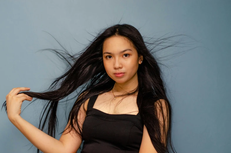 a young asian woman with long dark hair posing with her hands in the air and her hair flying in the wind