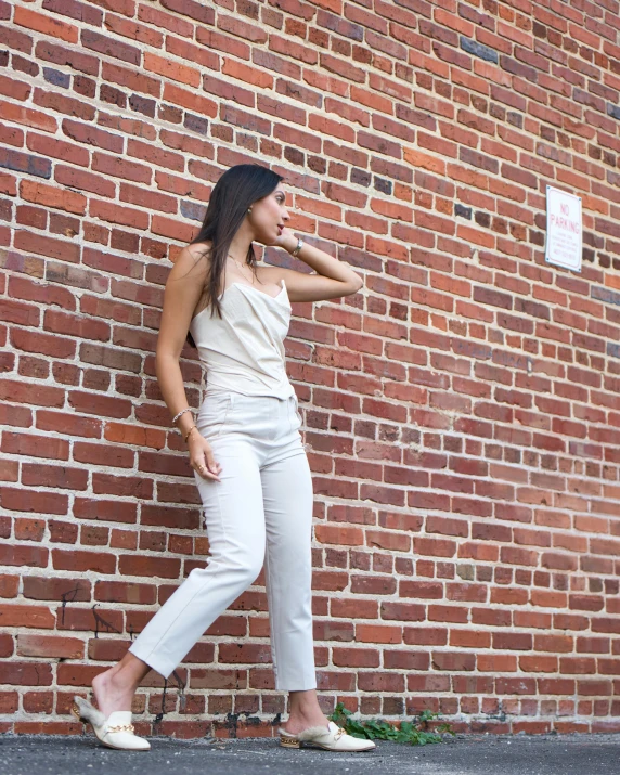 a woman leaning against a brick wall near the grass