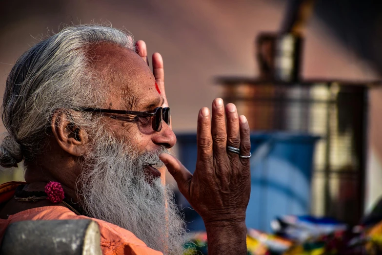 an elderly man with greying beard and red flowers on his left wrist holding his hands to the side