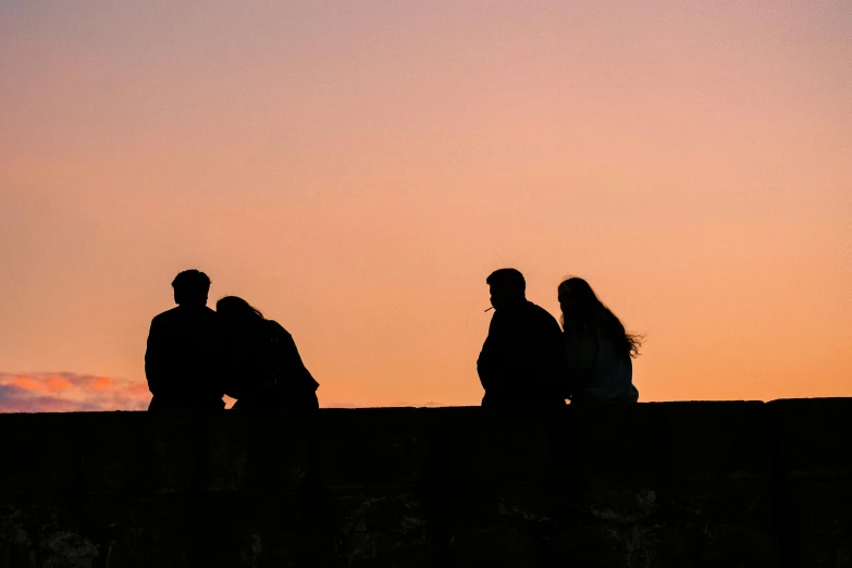 the silhouettes of three people sitting on the edge of a building