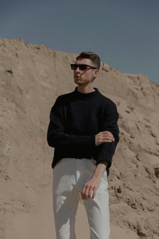 a man stands in front of a rock while wearing a black sweater