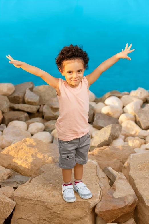 a girl holding her arms out while standing on rocks