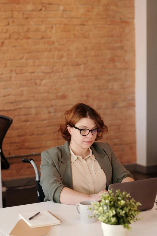 a woman in glasses sitting at a table with a laptop