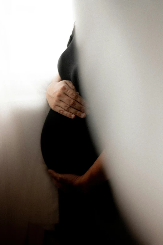 a pregnant woman leaning against a wall wearing a black dress