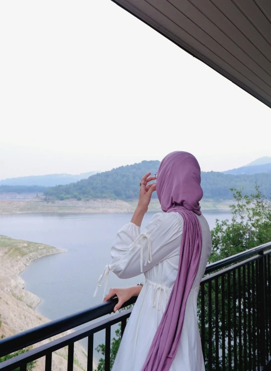 a woman in a purple headscarf stands at the edge of a balcony