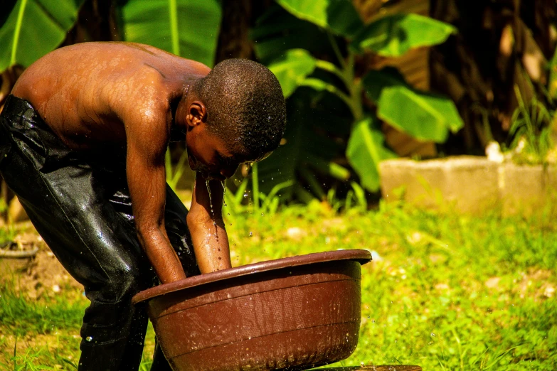 a young man is drinking water out of a bucket