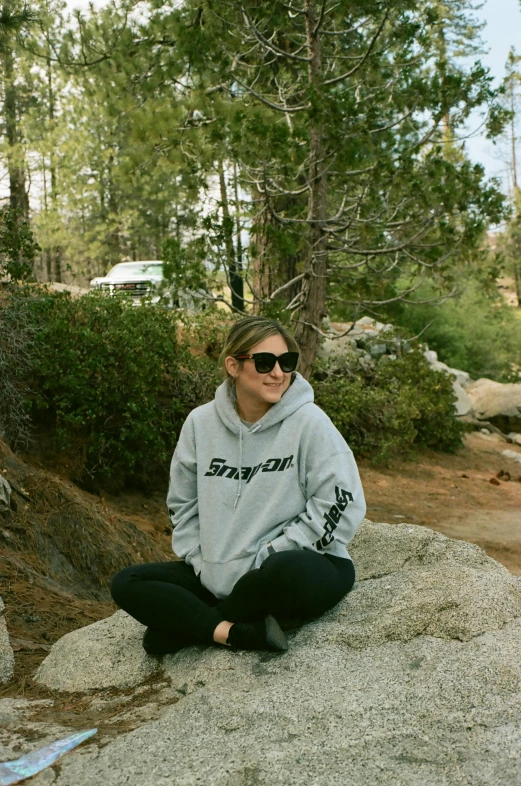 a woman sitting on a rock with sunglasses