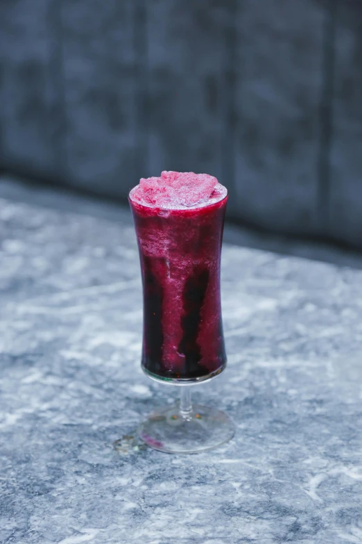 a small red drink on a table with a pink substance floating from it