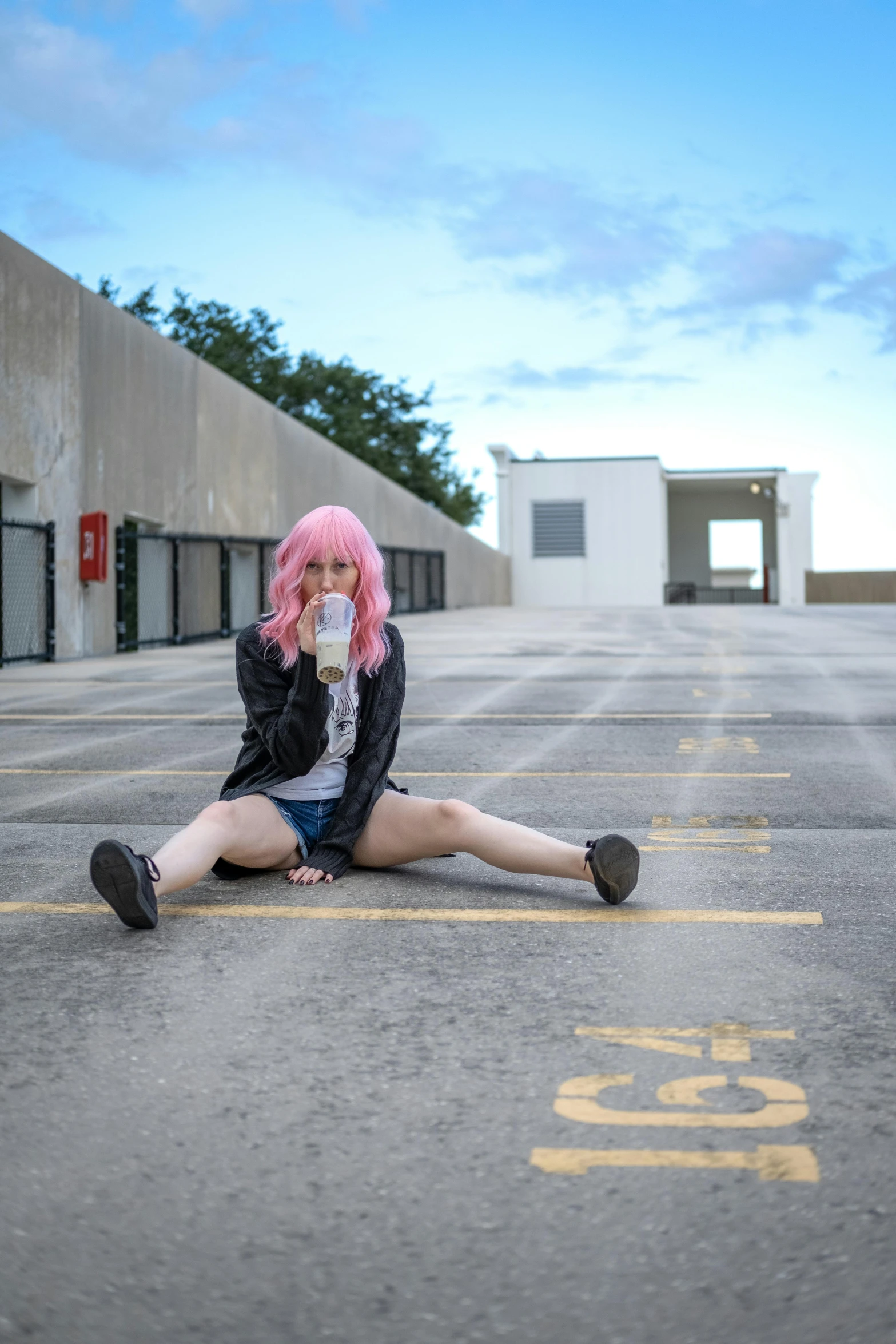 woman with pink hair sitting on the pavement with a cup