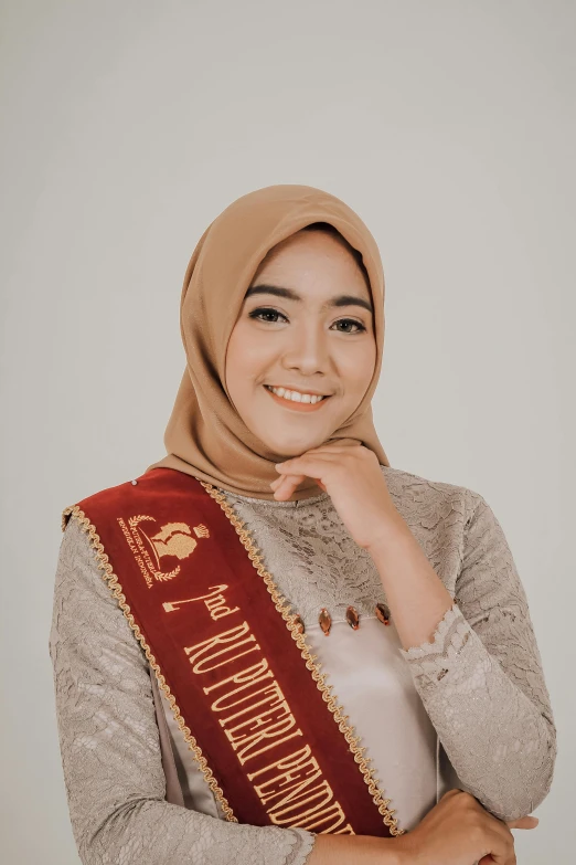 a woman wearing a hijab and a sash is posing for the camera