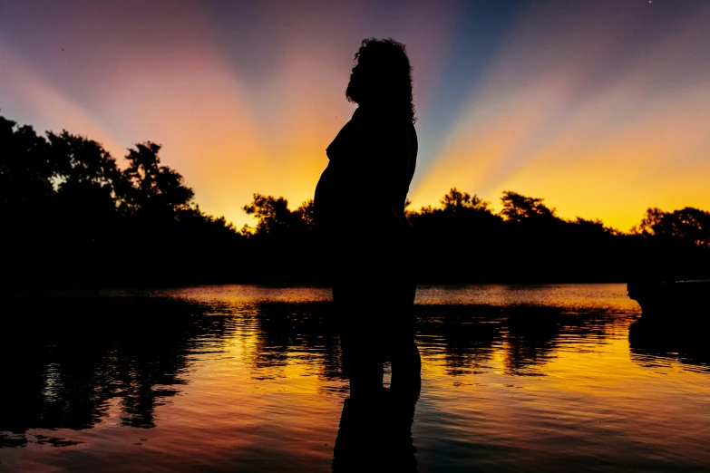 a person standing in the dark by water watching the sun go down