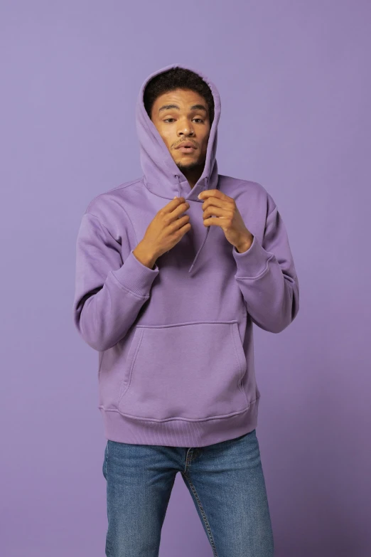a person wearing a purple hoodie stands against a lila background