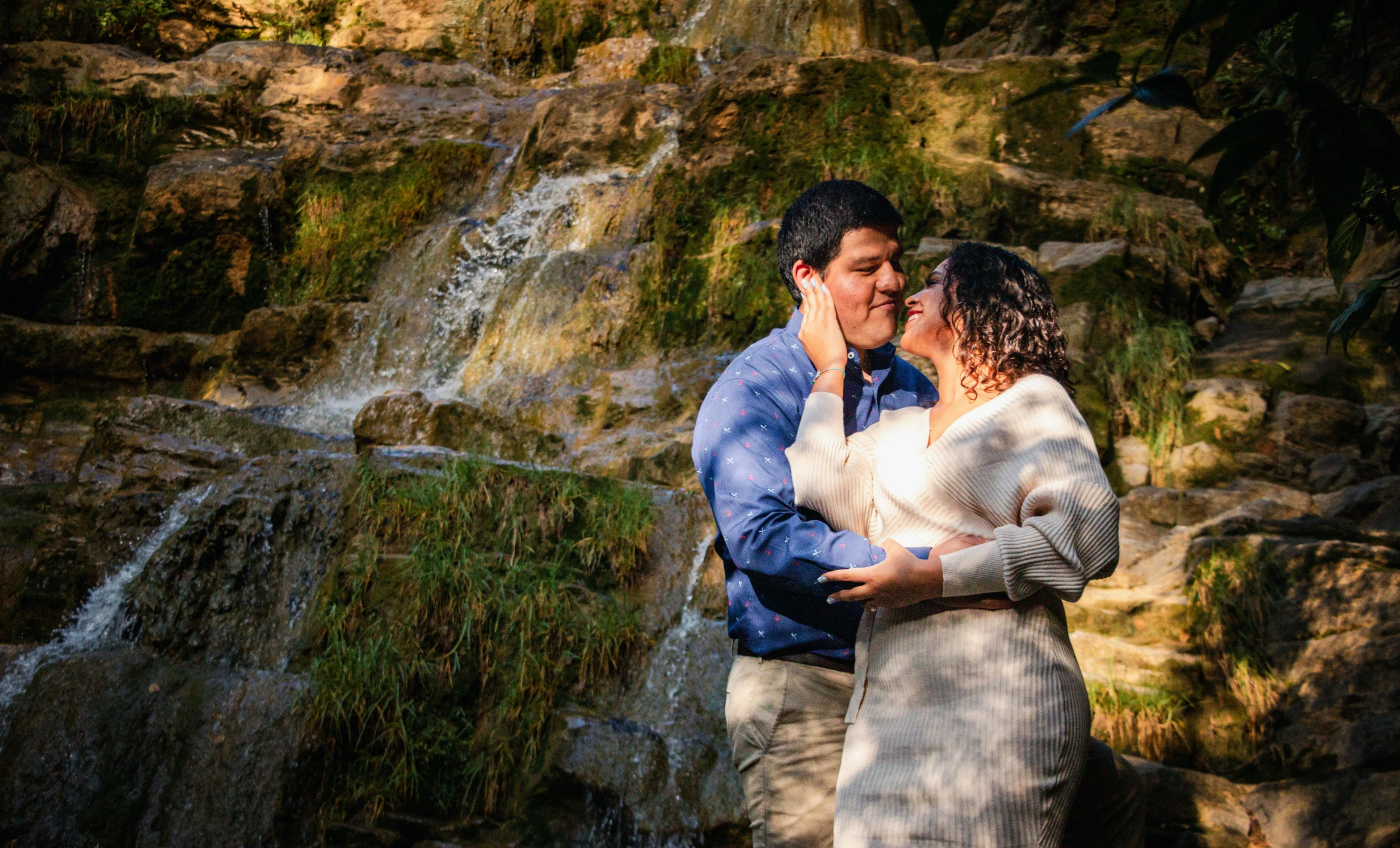 a man and woman emcing in front of a waterfall