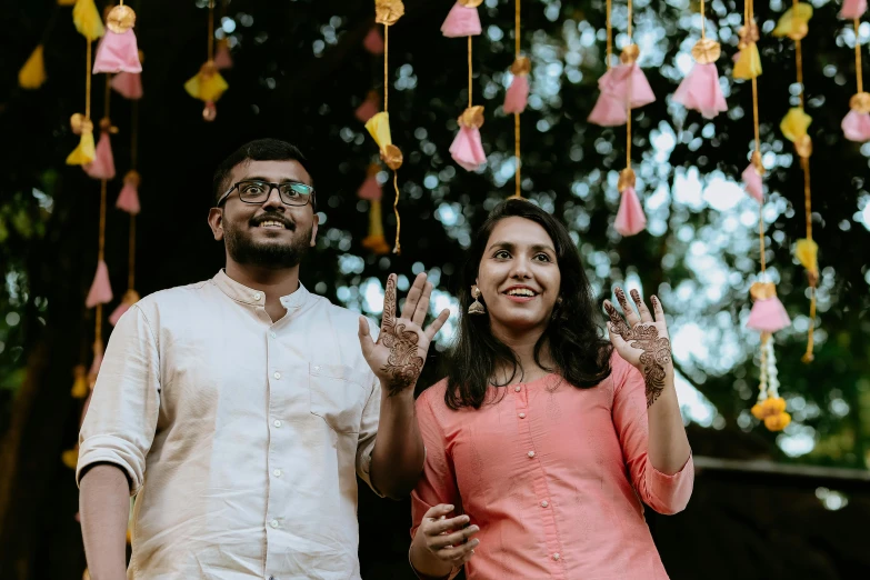 a smiling couple standing next to each other holding up their hand