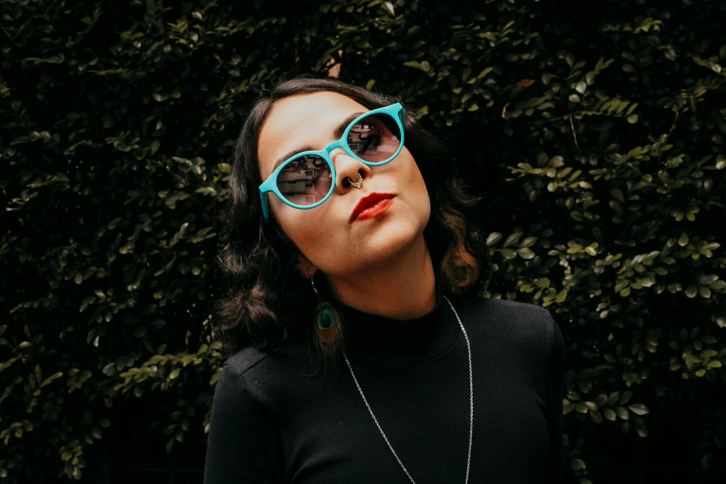 a woman wearing blue round glasses standing in front of green plants