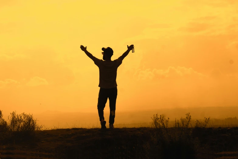 silhouette of man on top of hill with arms wide open in the sky