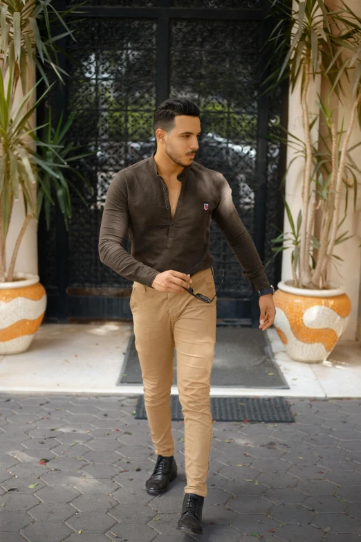 a man in tan pants stands outside wearing a black sweater and brown shoes