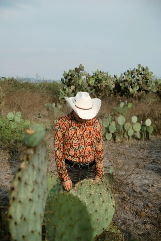 a man in cowboy hat standing by a cactus