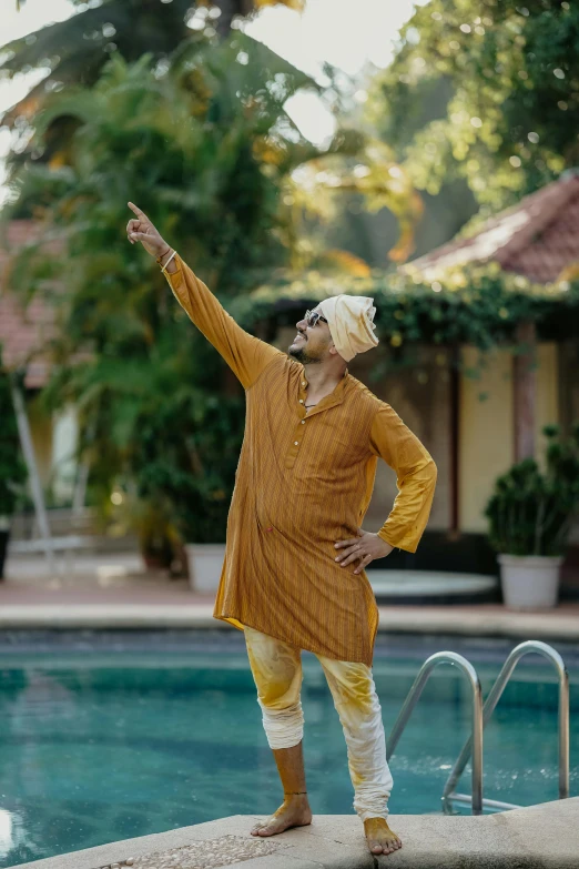 a man in a hat standing on the edge of a swimming pool, arms outstretched