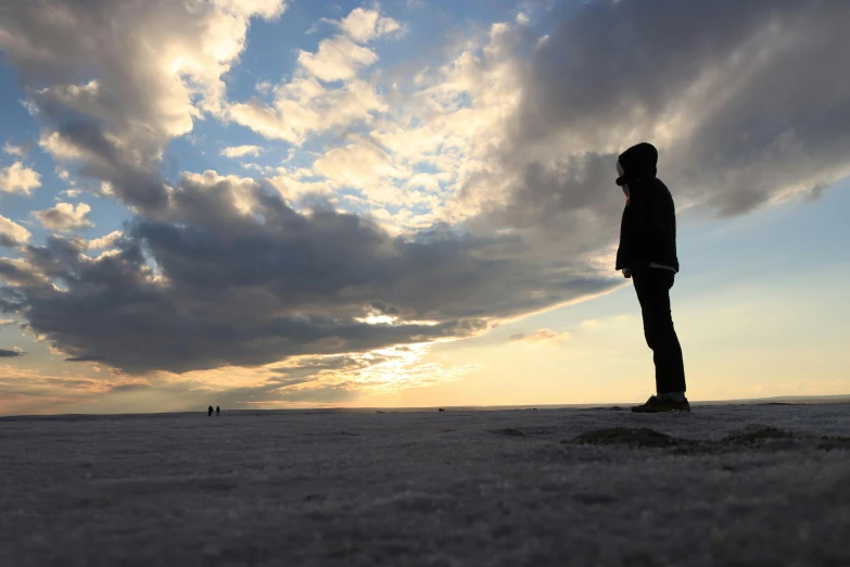 a person standing alone in an open plain under a blue and cloudy sky