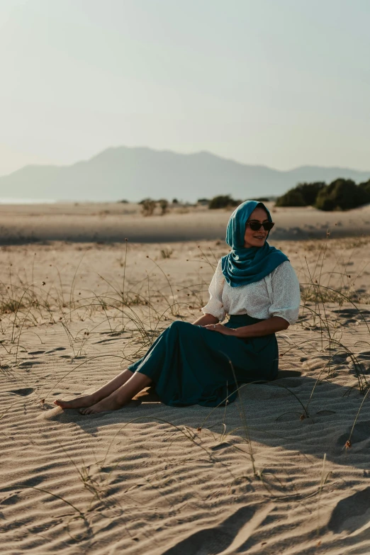 woman wearing glasses and blue scarf sitting on the beach