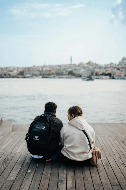 two people sitting next to each other on a pier near the water