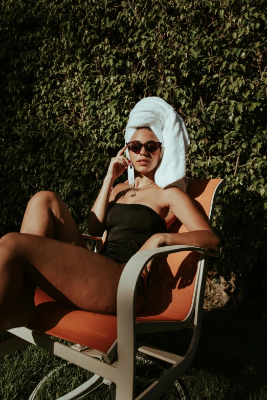 a young woman in glasses sits on a lawn chair and is talking on her cell phone