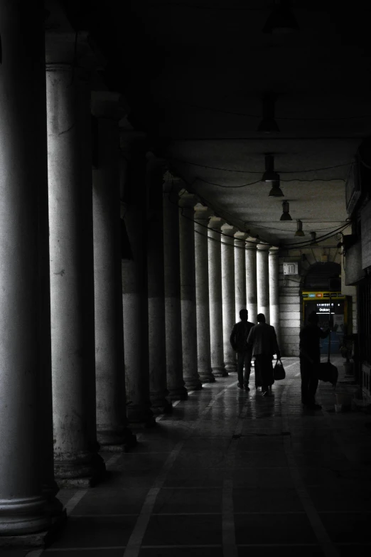 two people are walking in the dark under an arched columned walkway