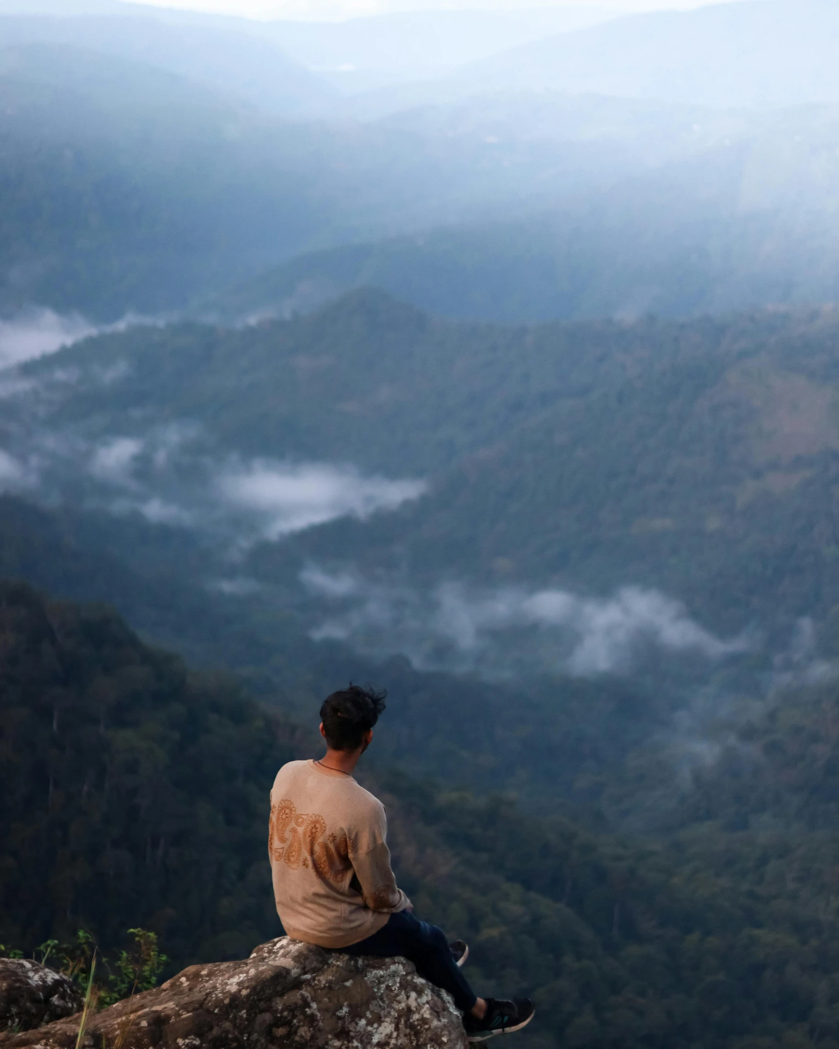 man sitting on a mountain overlooking valleys and clouds