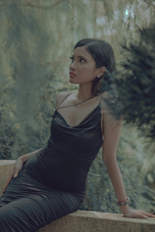 a woman is wearing a black dress and is sitting in the woods