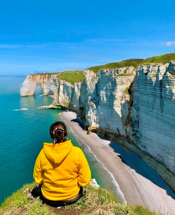 a person is sitting in a yellow jacket overlooking the water at cliffs