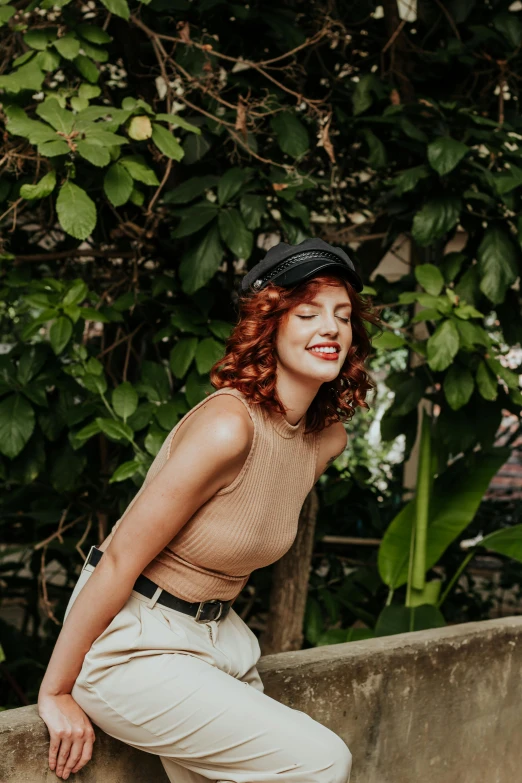 woman posing with hat on, leaning on wall