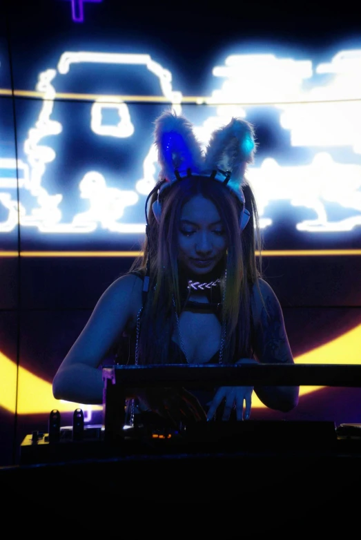 a woman wearing head phones sitting at a keyboard in front of a neon background