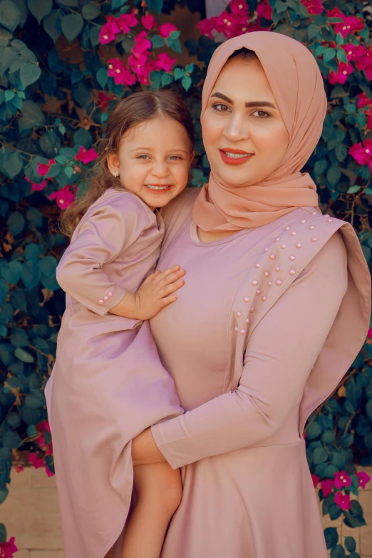 a mother and daughter pose together in front of a bush