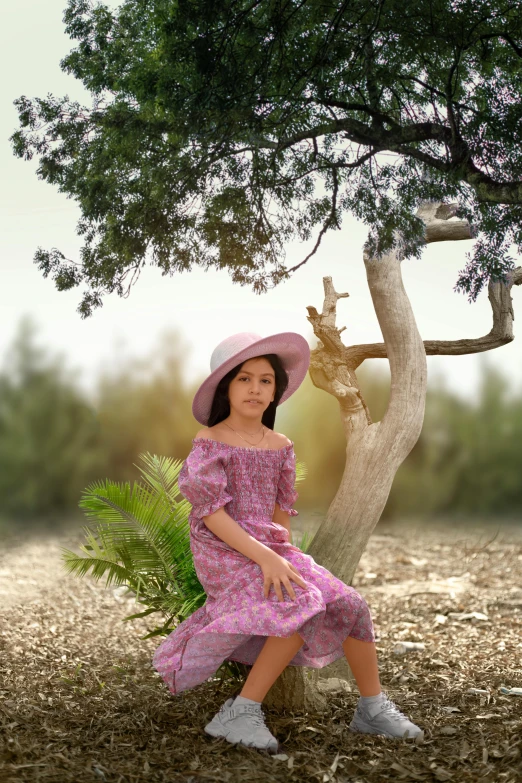 a  with pink dress and hat sits in front of a tree