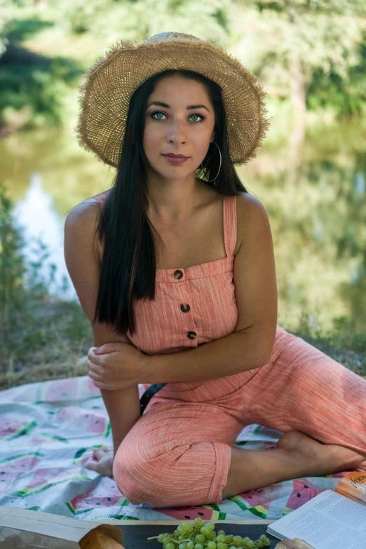 woman in straw hat and dress sitting on a picnic blanket with gs and bread