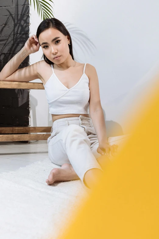 a beautiful young woman sitting on top of a floor next to a chair