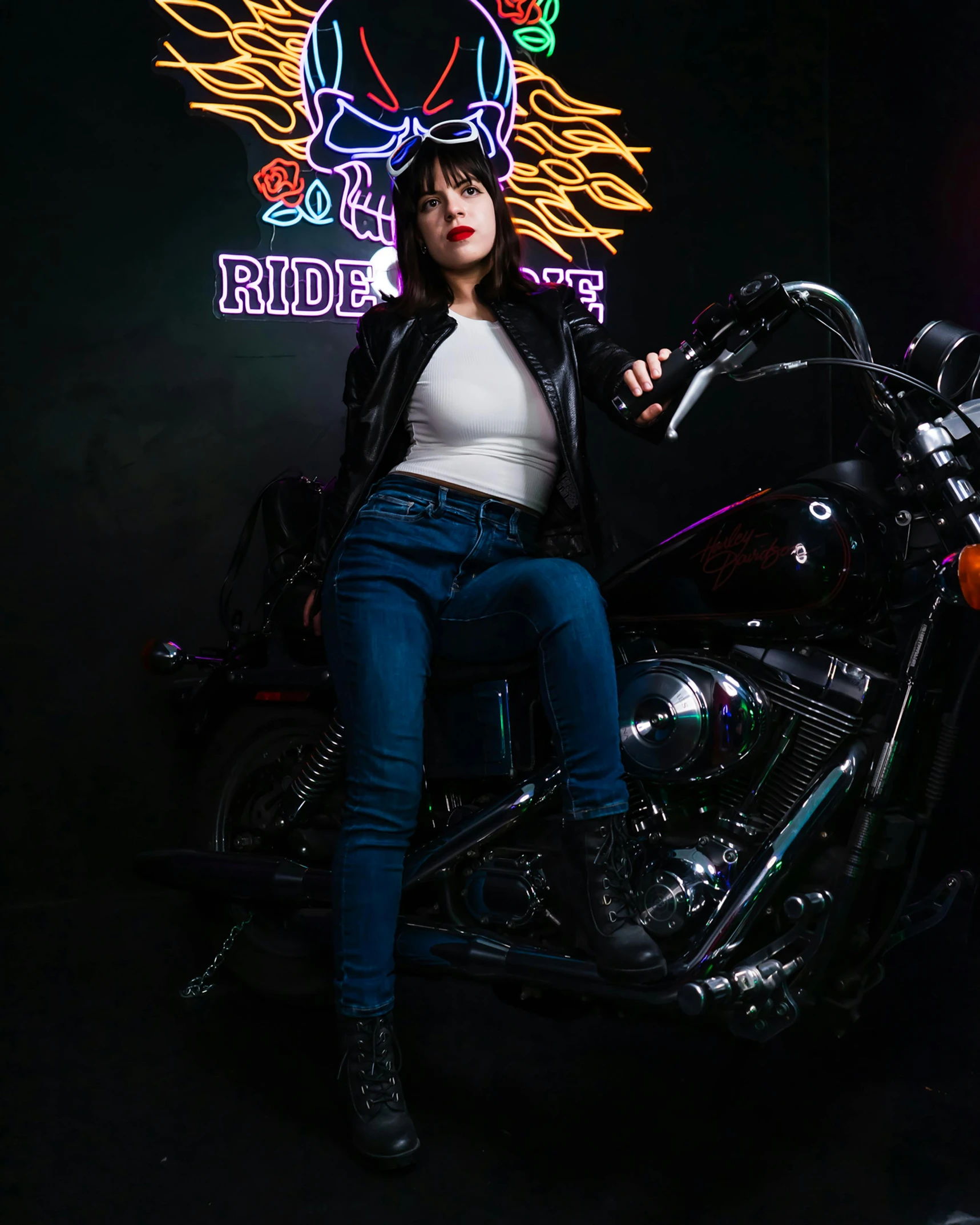 a woman sits on top of a motorcycle in front of a neon sign