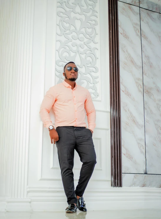 a man in pink shirt and sunglasses leaning against white marble wall