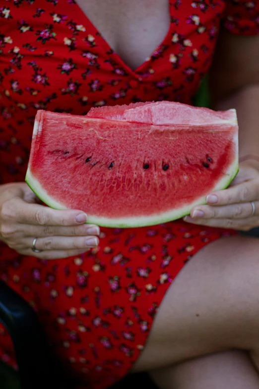 someone wearing red holding a piece of watermelon