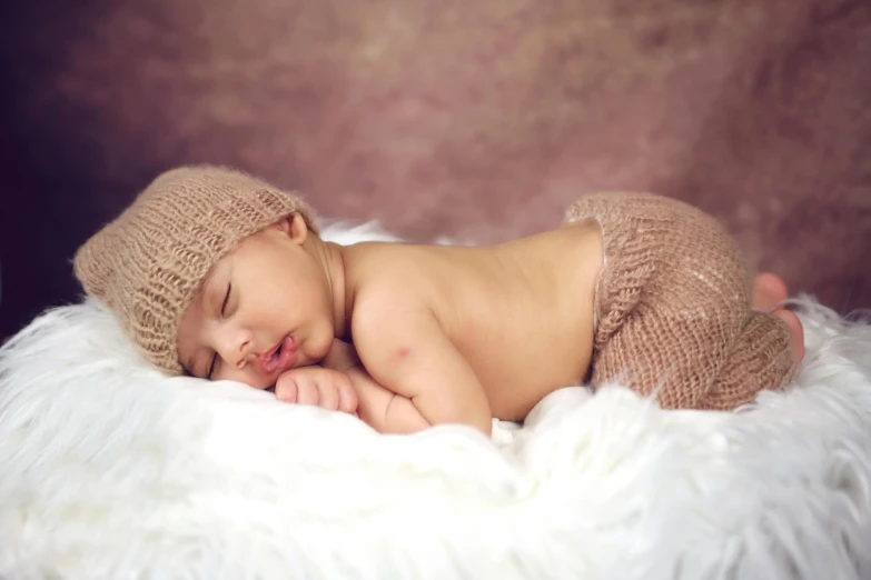 a baby in a sweater and cap sleeping on a fur blanket