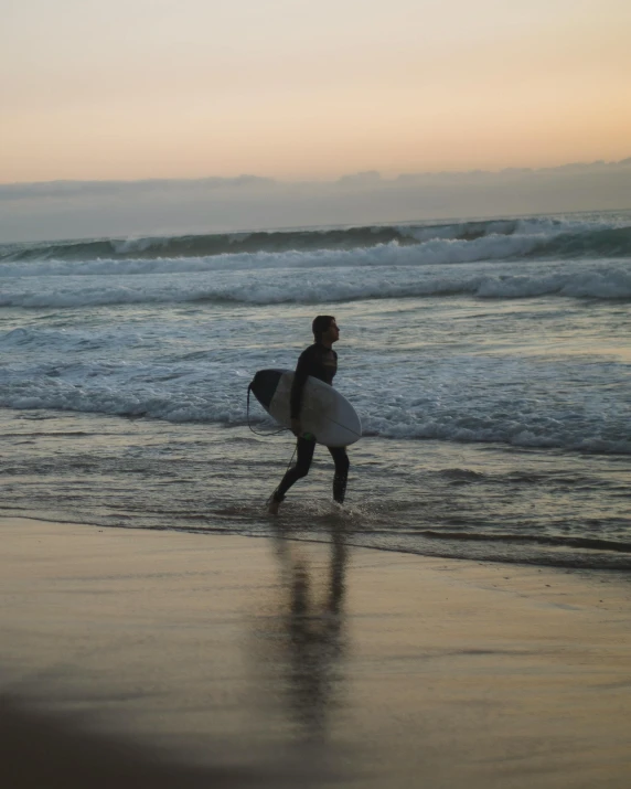 a man holding a surfboard walking along the shore of the beach