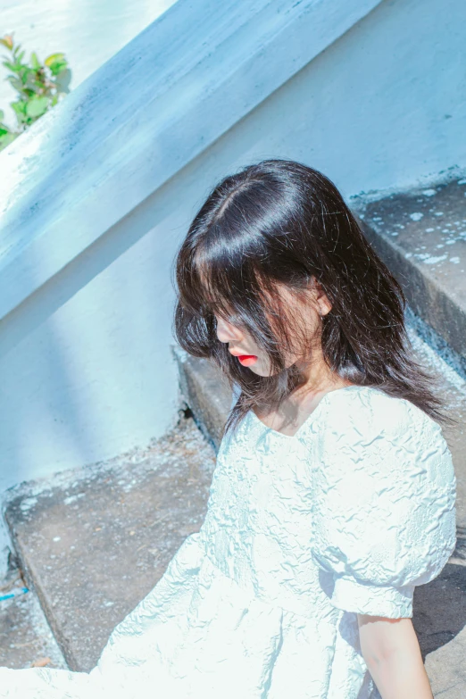 a close up view of the side of a woman with her hair curled in pony tail, sitting on a step near an enclosure