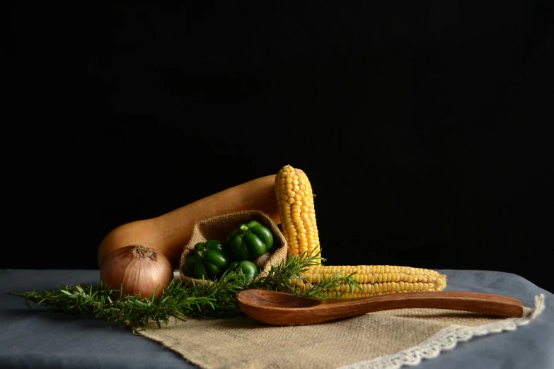 an onion, corn and a wooden spoon on a table