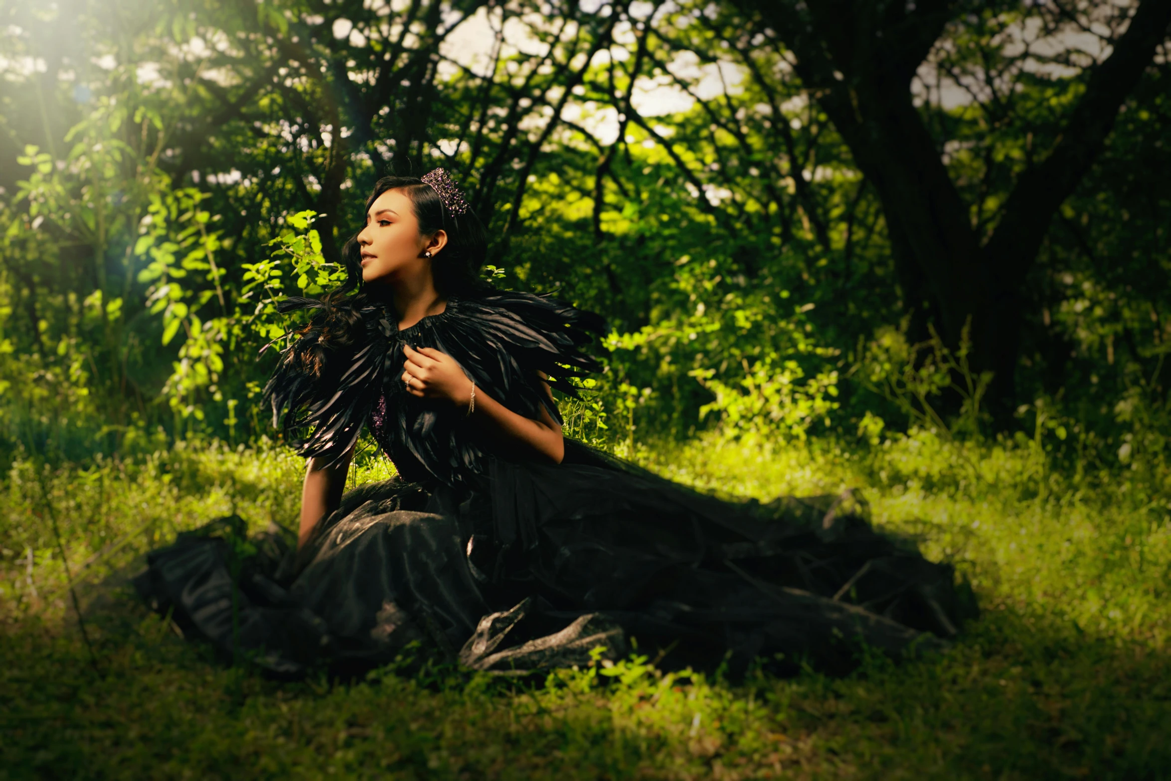 a woman sits on grass in front of some trees